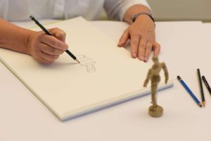 Mit einem Bleistift wird eine Gliederpuppe abgezeichnet