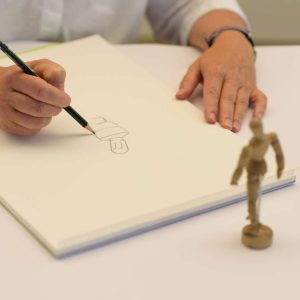 Mit einem Bleistift wird eine Gliederpuppe abgezeichnet