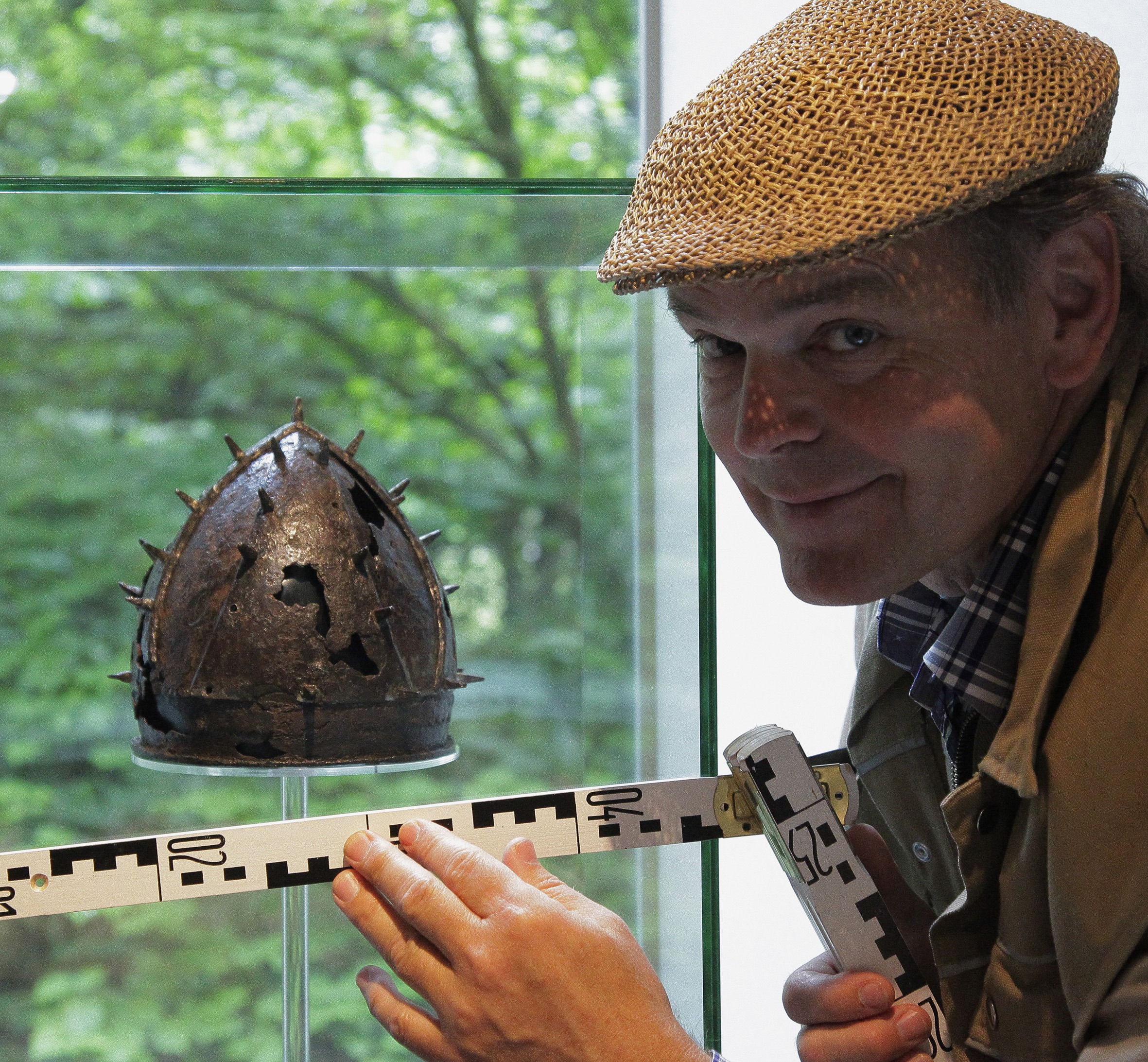 Pago Balke mit einer Mütze und einem Maßstock vor einem altem Helm.