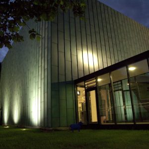 Foto des Schaumagazin von außen. Zu sehen ist ein grüner Kubus. Es ist dunkel und das Gebäude ist beleuchtet.