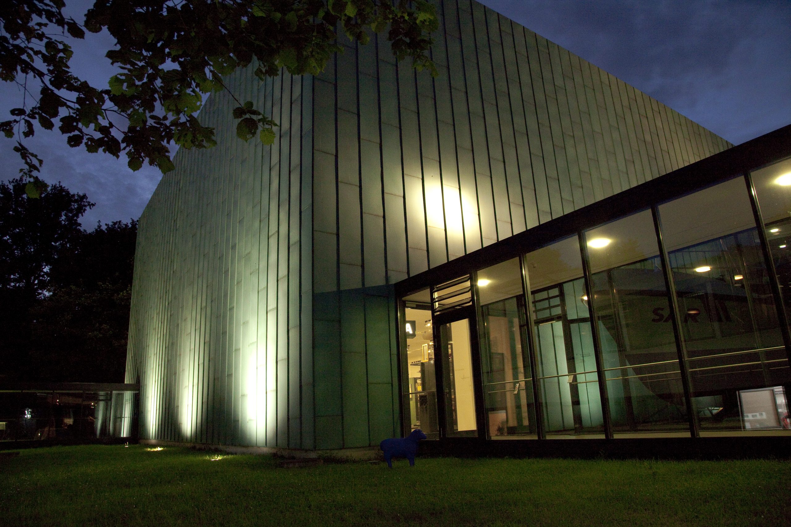 Foto des Schaumagazin von außen. Zu sehen ist ein grüner Kubus. Es ist dunkel und das Gebäude ist beleuchtet.