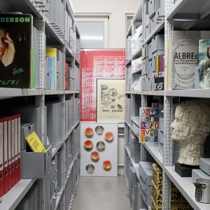 Archivregalreihen mit Büchern, Skulpturen, Schallplatten und Ordnern